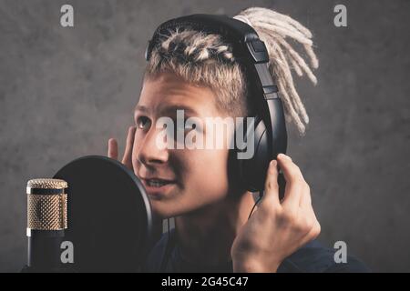 Ein glücklicher positiver Kerl mit Dreadlocks zeichnet im Studio einen Song auf. Ein junger, attraktiver Sänger in schwarzen Studio-Kopfhörern steht vor einem Mikrop