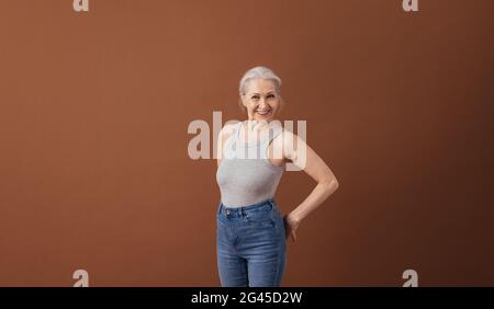 Porträt einer reifen Frau in Casuals, die auf braunem Hintergrund im Studio steht Stockfoto