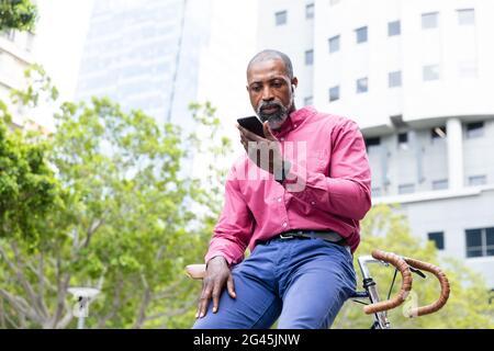 Afroamerikanischer Mann sitzt auf seinem Fahrrad und benutzt sein Telefon Stockfoto