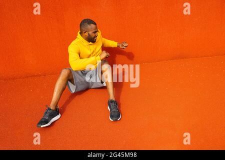 Konzentrierter afroamerikanischer Sportler sitzt und macht Aufwärmtraining vor dem Fußballspiel, Basketballspiel, macht sich bereit, hält fit und Stockfoto