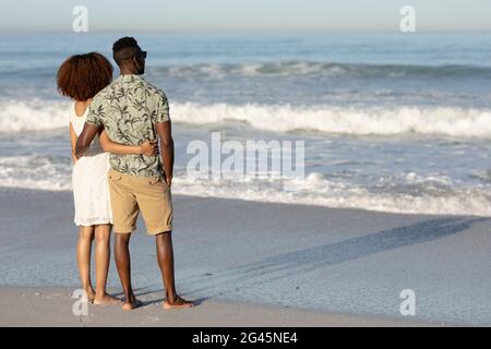 Ein gemischtes Rennpaar bewundert die Aussicht und hält sich am Strand Stockfoto