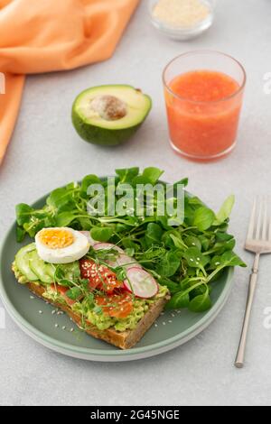 Gesundes, leckeres Frühstück, Sandwich mit Avocado und Lachs, Gurken und Radieschen sowie Mikrogemüse aus Erbsen mit gekochtem Ei und Maissalat Stockfoto