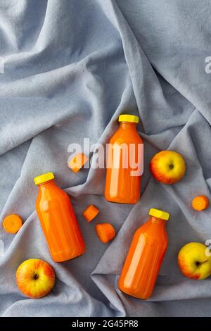 Karotten-Apfelsaft in Flaschen mit frischen Äpfeln und Karotten auf blauer Tischdecke, Draufsicht Stockfoto