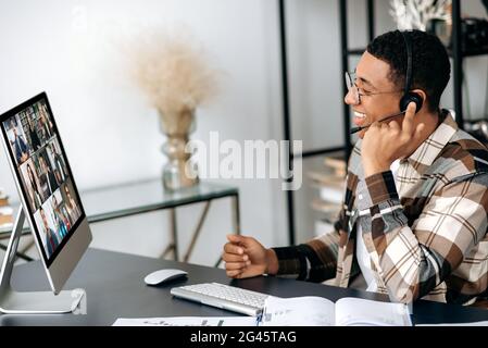 Virtuelles Geschäftstreffen, Online-Beratung. Selbstbewusster Latino-Mann mit einem Headset, der mit Geschäftspartnern kommuniziert, ein Projekt diskutiert, eine Konsultation durchführt, multiethnische Menschen auf einem Bildschirm Stockfoto