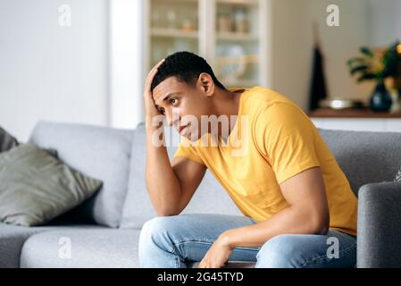 Trauriger, unglücklicher, gutaussehender junger mann aus hispanic, der zu Hause auf dem Sofa sitzt, seine Stirn hält, Kopfschmerzen, Depressionen hat, enttäuscht, Braucht psychologische Unterstützung Stockfoto