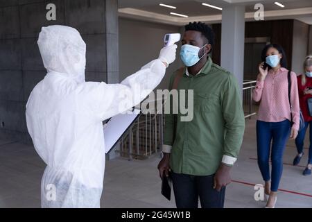 Gesundheitsarbeiter trägt Schutzkleidung Überprüfung der Temperatur des Geschäftsmannes Stockfoto