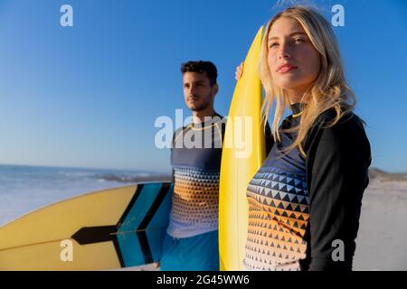 Kaukasisches Paar hält Surfbretter am Strand. Stockfoto