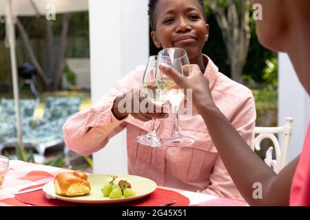 Ältere afroamerikanische Frau und ihre Familie machen einen Toast mit Wein zusammen im Garten Stockfoto