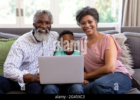 Gemischter Rennjunge und seine Großeltern mit einem Laptop auf einer Couch sitzen Stockfoto