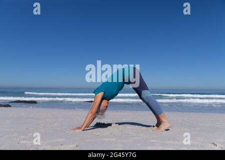 Ältere kaukasische Frau, die am Strand Yoga praktiziert. Stockfoto