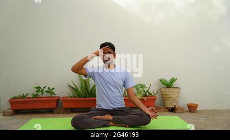 Heiterer indischer Kerl, der im Freien Yoga praktiziert. Junge Yogapraktikerin, die mit geschlossenen Augen in Lotushaltung arbeitet und sitzt. Yoga und Meditation concep Stockfoto