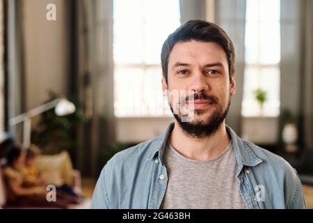 Fröhlicher junger Mann in Casualwear, der Sie im Wohnzimmer ansieht Stockfoto