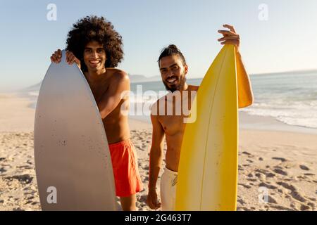 Junge Männer mit gemischtem Rennen halten Surfbretter am Strand Stockfoto