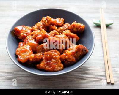 chinesische Küche: Süßes und saures Schweinefleisch (guo bao rou) in einer grauen Schüssel auf einem Holztisch Stockfoto