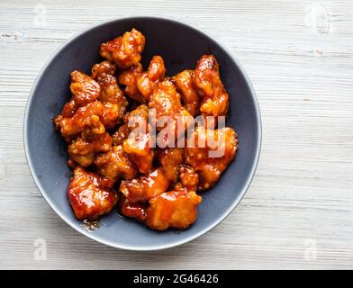 chinesische Küche – Blick von oben auf das süss-saure Schweinefleisch (guo bao rou) in einer grauen Schüssel auf dem Holztisch Stockfoto