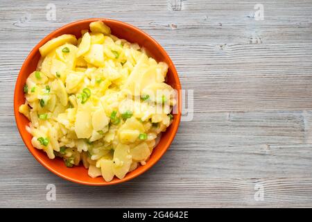 Blick von oben auf den Kartoffelsalat in einer orangefarbenen Schüssel auf einem grauen Holztisch Stockfoto