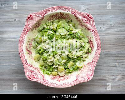 Draufsicht auf Salat mit Trauben, Estragon und Huhn in Zierschale auf grauem Holztisch Stockfoto