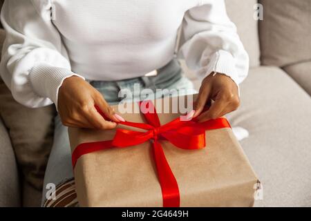 Weihnachtlicher Lifestyle und Shopping und Black friday Konzept. Nahaufnahme Hände der afroamerikanischen jungen Frau öffnet Box mit weihnachtsgeschenk mit rot Stockfoto