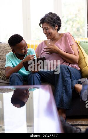 Gemischter Rennjunge und seine Großmutter mit digitalen Tablet sitzen auf einer Couch Stockfoto