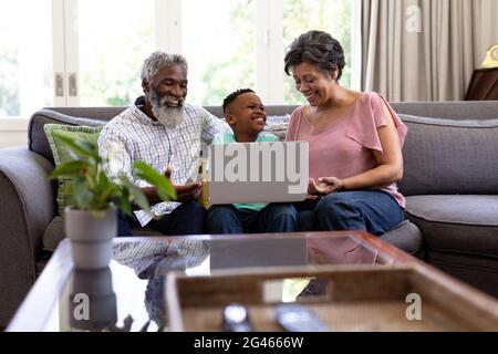 Gemischter Rennjunge und seine Großeltern mit einem Laptop auf einer Couch sitzen Stockfoto