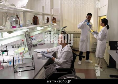 Gruppe interkultureller Wissenschaftler in Whitecoats und Handschuhen, die im Labor arbeiten Stockfoto