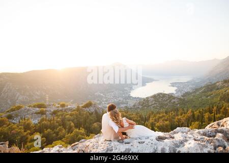 Braut und Bräutigam umarmen sich auf dem Berg Lovcen, vor ihnen öffnet sich ein malerischer Panoramablick auf die Bucht von Kotor Stockfoto