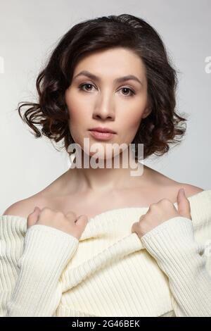 Brunette schöne Frau in großen weißen Wollpullover auf grauem Hintergrund gekleidet. Stockfoto