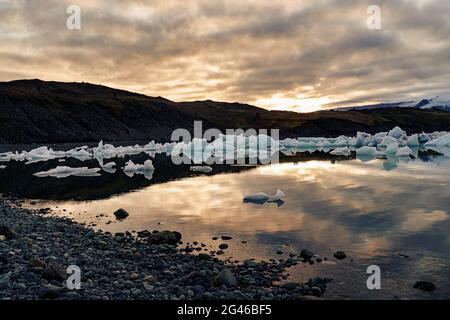 Die Eisberge, die in der Dämmerung in der Lagune dahintreiben, während die Sonne hinter der Bergkette untergeht. Jokulsarlon, Island Stockfoto