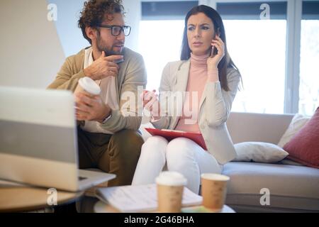 Eine Geschäftsfrau, die auf ihrem Handy telefoniert, verwirrt und besorgt aussieht, und ihre Kollegin neben ihr sitzt Stockfoto