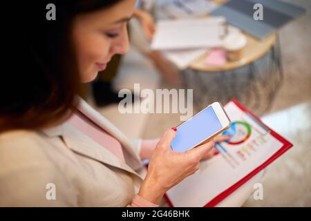 Draufsicht über die Schulter der jungen kaukasischen Brünette hält und schaut ihr Handy. Stockfoto