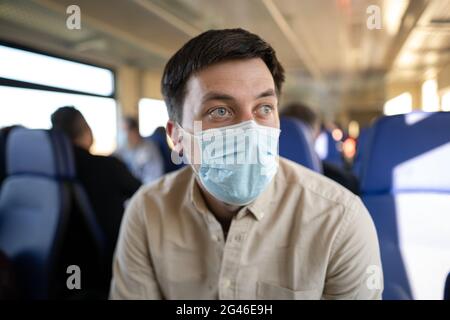 Mann, der mit dem Zug unterwegs ist und eine Gesichtsmask trägt. Soziale Distanzierung bei Bahnreisen während der Covid-19-Pandemie. Männlich pendeln nach Stockfoto