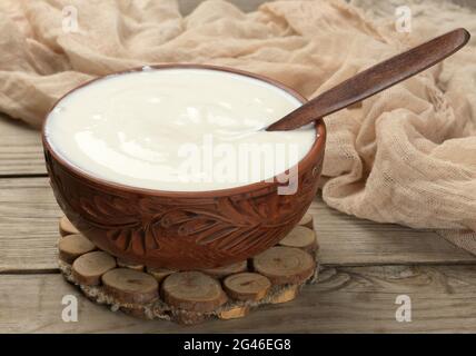 Saure Creme in einer braunen Keramikschale mit einem Holzlöffel auf einem hölzernen Hintergrund, fermentierte Milch nützliches Produkt Stockfoto