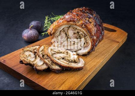 Traditionelles italienisches Schweinefleisch Porchetta arrotolata in Scheiben geschnitten und als Stück mit Kräutern und Feigen als Nahaufnahme auf einem modernen Design angeboten Stockfoto