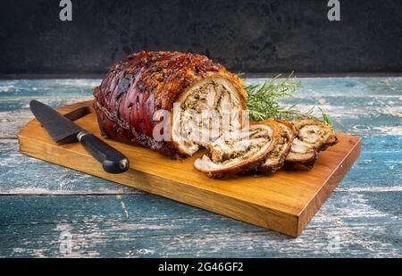 Traditionelles italienisches Schweinefleisch Porchetta arrotolata in Scheiben geschnitten und als Stück mit Kräutern als Nahaufnahme auf einem modernen Design aus Holz angeboten Stockfoto