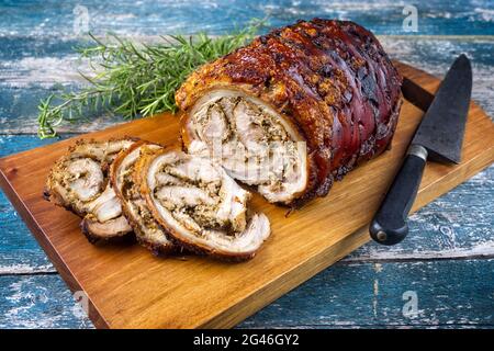 Traditionelles italienisches Schweinefleisch Porchetta arrotolata in Scheiben geschnitten und als Stück mit Kräutern als Nahaufnahme auf einem modernen Design aus Holz angeboten Stockfoto