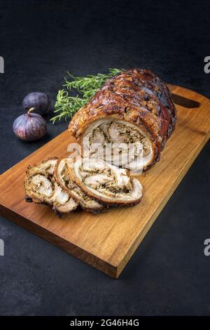 Traditionelles italienisches Schweinefleisch Porchetta arrotolata in Scheiben geschnitten und als Stück mit Kräutern und Feigen als Nahaufnahme auf einem modernen Design angeboten Stockfoto