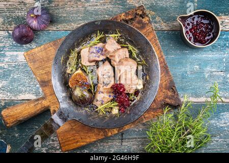 Traditionelle gekochte Kalbszungenscheiben Feigen und Preiselbeeren, die als Draufsicht in einer rustikalen gusseisernen Pfanne auf einem alten hölzernen bo angeboten werden Stockfoto