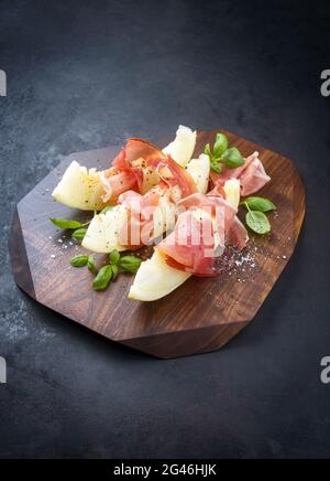 Traditionelle italienische Antipasti mit Prosciutto di Parma und Honigmelonen-Scheiben, die als Nahaufnahme auf einem Holzbrett angeboten werden Stockfoto