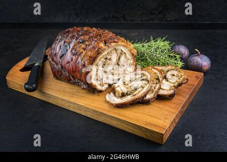 Traditionelles italienisches Schweinefleisch Porchetta arrotolata in Scheiben geschnitten und als Stück mit Kräutern und Feigen als Nahaufnahme auf einem modernen Design angeboten Stockfoto