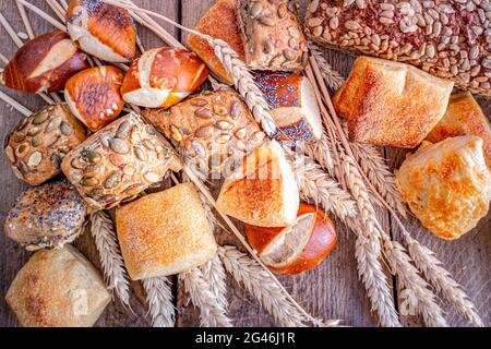 Eine große Auswahl an frisch gebackenen Brötchen auf einem rustikalen Holzhintergrund mit einem Weizenbündel Stockfoto