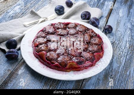 Traditionelle französische Tarte aux prunes mit süßen Pflaumen und Vanille, die als Nahaufnahme auf einem klassischen Design-Teller mit rustikalem Holz angeboten wird Stockfoto