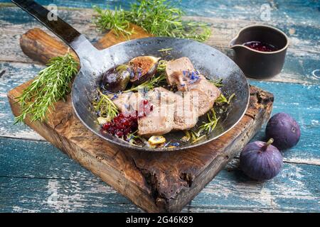 Traditionelle gekochte, in Scheiben geschnittene Kalbszungenfeigen und Preiselbeeren werden als Nahaufnahme in einer rustikalen gusseisernen Pfanne auf einem alten hölzernen bo angeboten Stockfoto