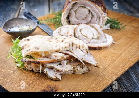 Traditionelles italienisches Schweinefleisch Porchetta arrotolata in Scheiben geschnitten und als Stück mit Pita-Brot und Rucola als Nahaufnahme auf einem angeboten Stockfoto