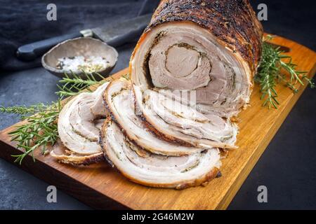 Traditionelles italienisches Schweinefleisch Porchetta arrotolata in Scheiben geschnitten und als Stück mit Kruste in Nahaufnahme auf einem modernen Holzdesign angeboten Stockfoto