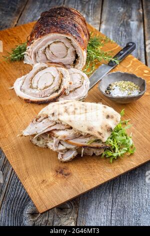 Traditionelles italienisches Schweinefleisch Porchetta arrotolata in Scheiben geschnitten und als Stück mit Pita-Brot und Rucola als Nahaufnahme auf einem angeboten Stockfoto