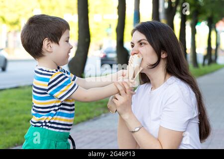 Ein kleiner Junge füttert seine Mutter mit einem Shaurma auf der Straße. Werbung für Fast Food und Street Food. Stockfoto