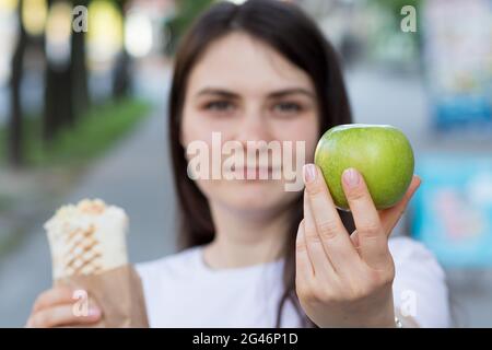 Junge schöne Brünette Frau auf einer Diät wählt Nahrung - was einen Apfel oder Fast-Food-Shawarma zu essen. Beißt den Apfel und wählt die richtige Ernährung. Stockfoto