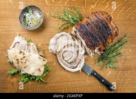 Traditionelles italienisches Schweinefleisch Porchetta arrotolata in Scheiben geschnitten und als Stück mit Pita-Brot und Rucola als Nahaufnahme auf einem angeboten Stockfoto