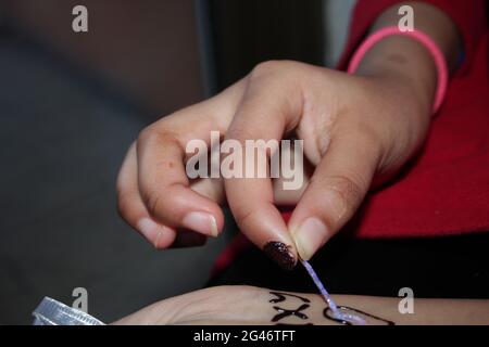 Zeichne den Henna menhdi-Text auf die Hand eines Mädchens. Stockfoto