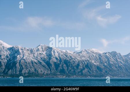 Schneebedeckte Berggipfel in der Bucht von Kotor, Montenegro, oberhalb der Stadt Dobrota. Eine assistable und Fischfarm im Meer. Stockfoto